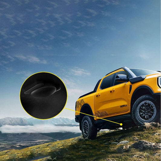 A composite image showing a bright yellow pickup truck (likely a Ford Ranger) parked on a rugged hillside against a backdrop of blue sky and mountainous scenery. A magnified black circular inset, connected by a yellow line to the underside of the pickup, provides a close-up view of a small, black car accessory, suggesting it is a GPS tracker (or similar discreet device).